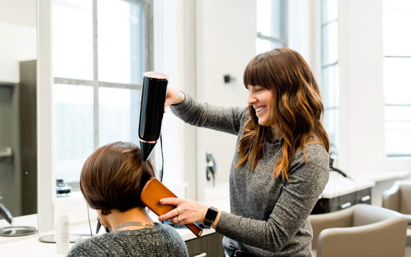Cabeleireira finalizando o cabelo de uma cliente no salão